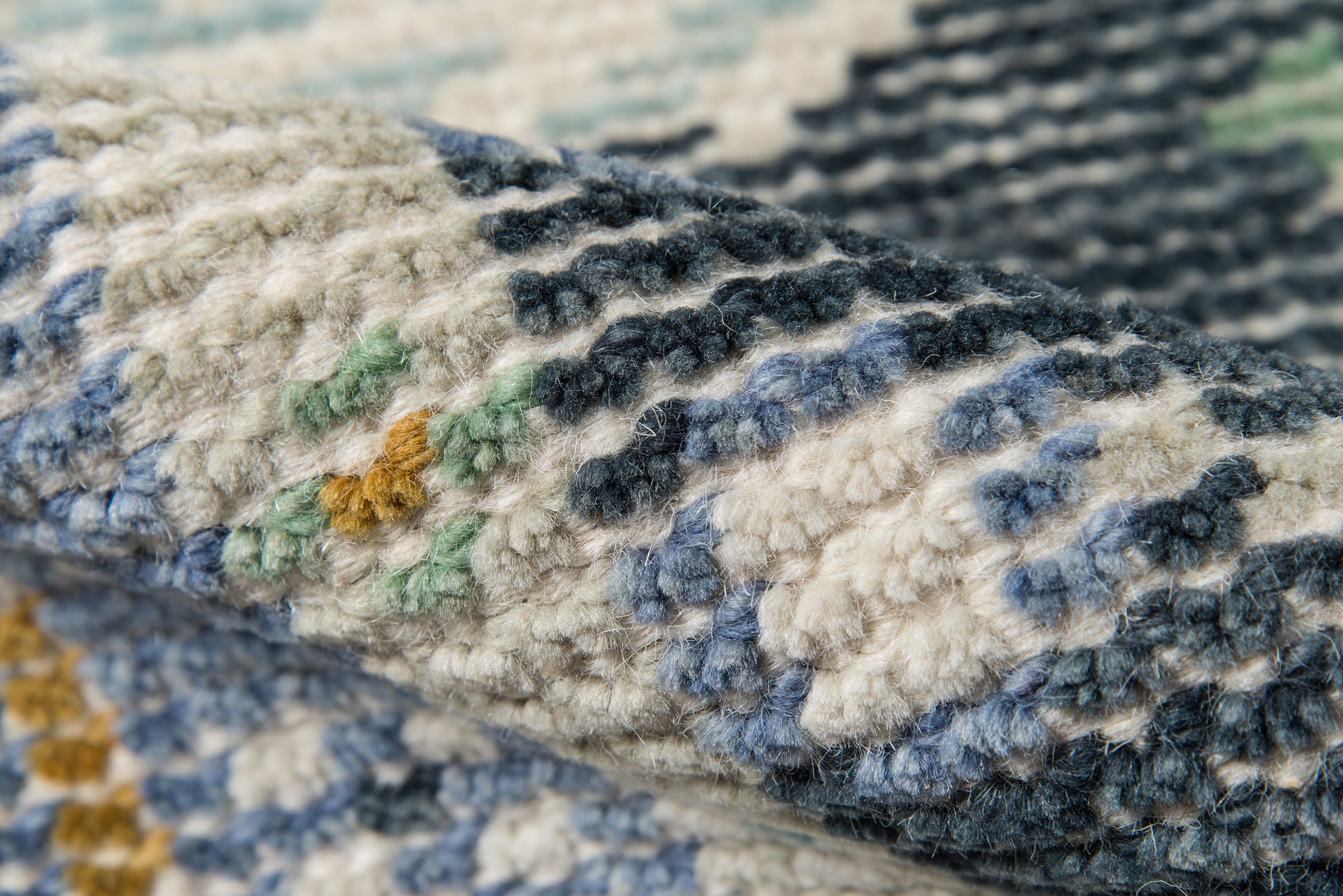 Close-up of a chunky knit textile with navy, cream and blue chevron stripes and small green/yellow flecks.