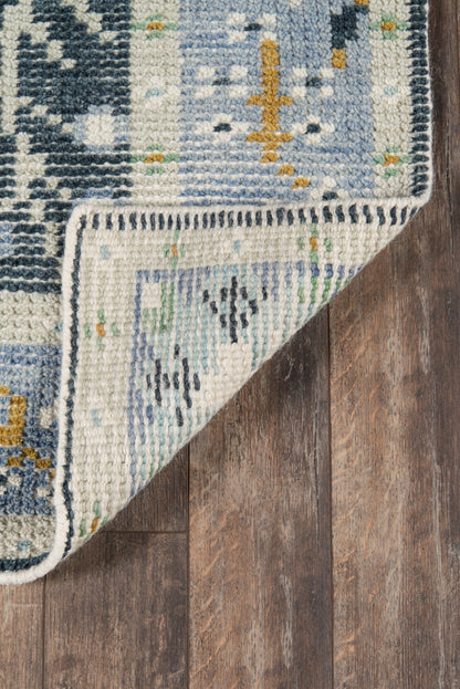 Blue and cream geometric rug with fringe, folded corner showing underside on a wooden floor.