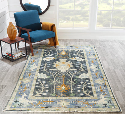 Blue-ivory geometric rug with mustard accents on light wood floor; teal armchair with wooden arms, an orange throw, and a side table in the scene.