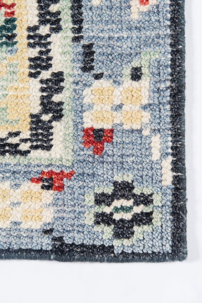 Blue tufted rug corner with light blue field, yellow and red floral-geometric motifs, dark blue border; thick pile.