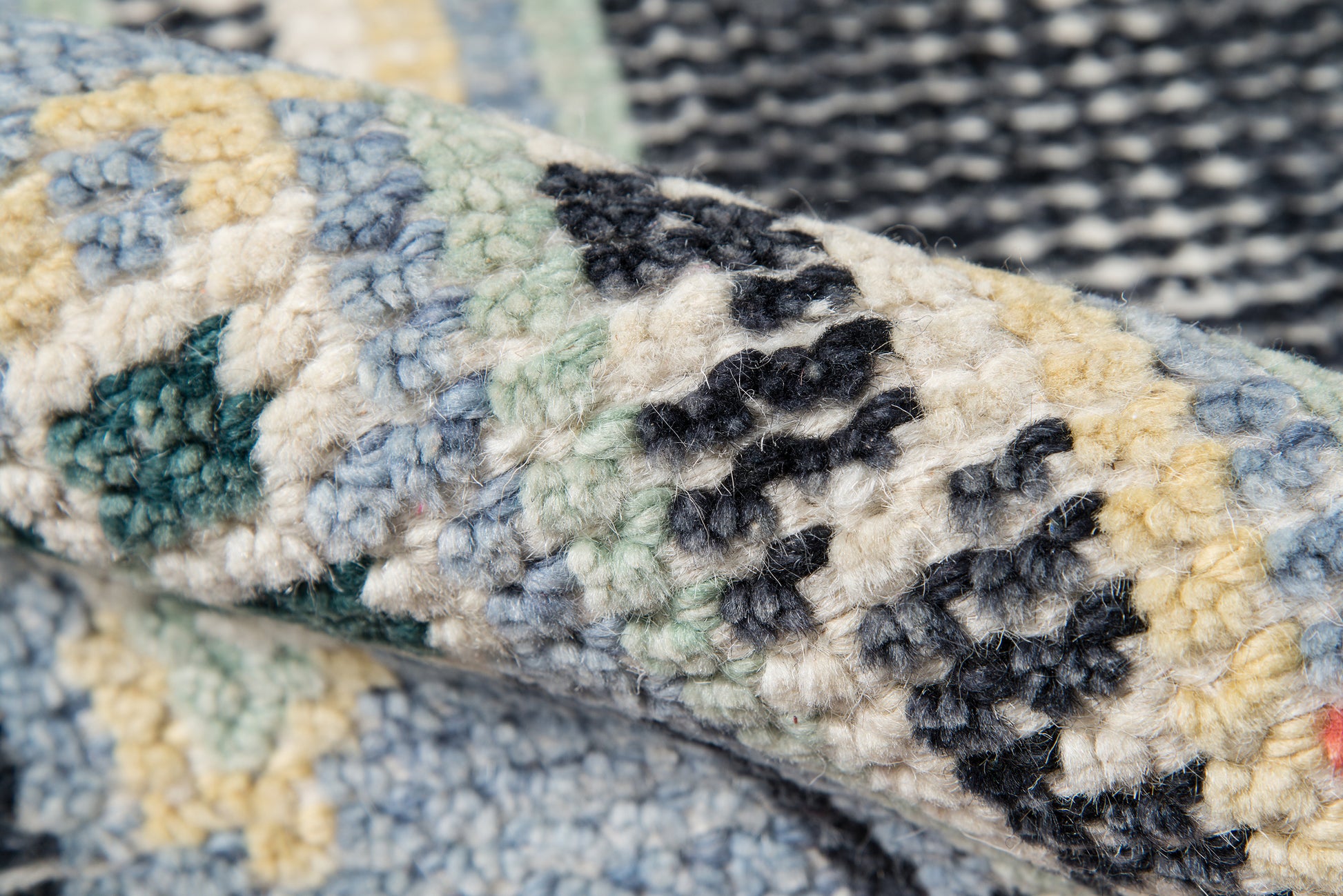 Close-up of a plush, tufted rug with blue, cream, black, and green patches in a geometric mosaic pattern.