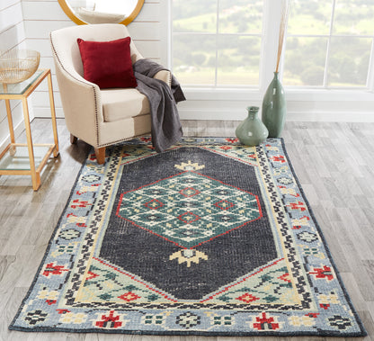 Geometric kilim-style rug with navy field and teal diamond medallion, framed by blue, cream and red tribal motifs.