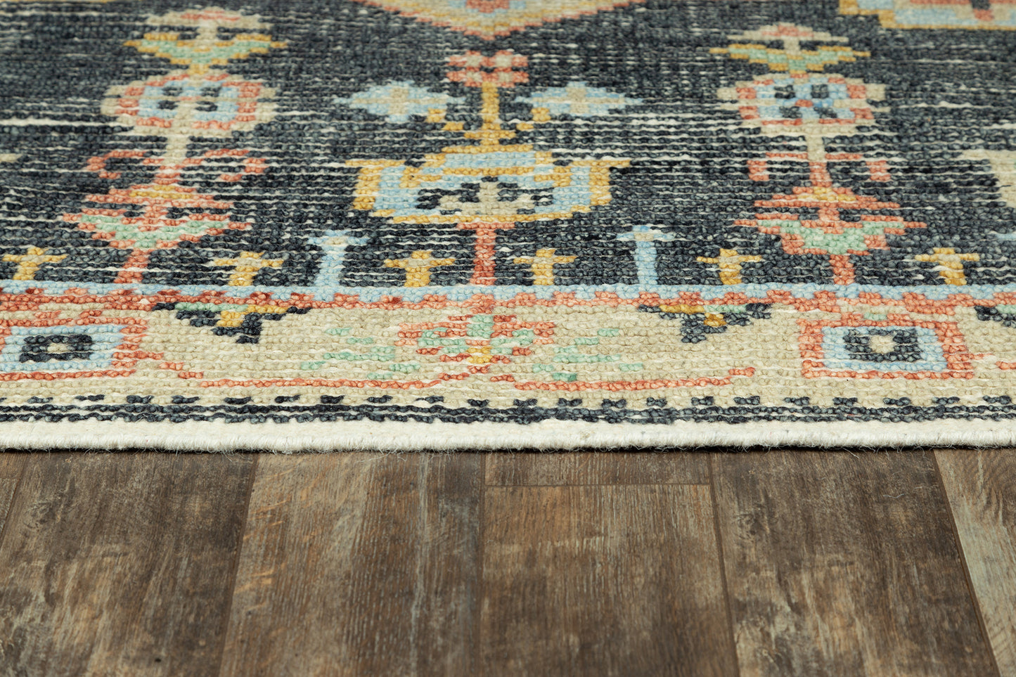 Close-up of an oriental rug with blue & orange & cream geometric motifs on a dark field over wood flooring.