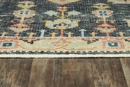 Close-up of an oriental rug with blue & orange & cream geometric motifs on a dark field over wood flooring.
