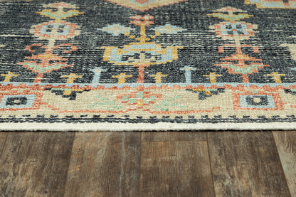 Dark navy oriental-style rug with geometric ivory, teal, peach and orange motifs on a wood floor; fringed edge.