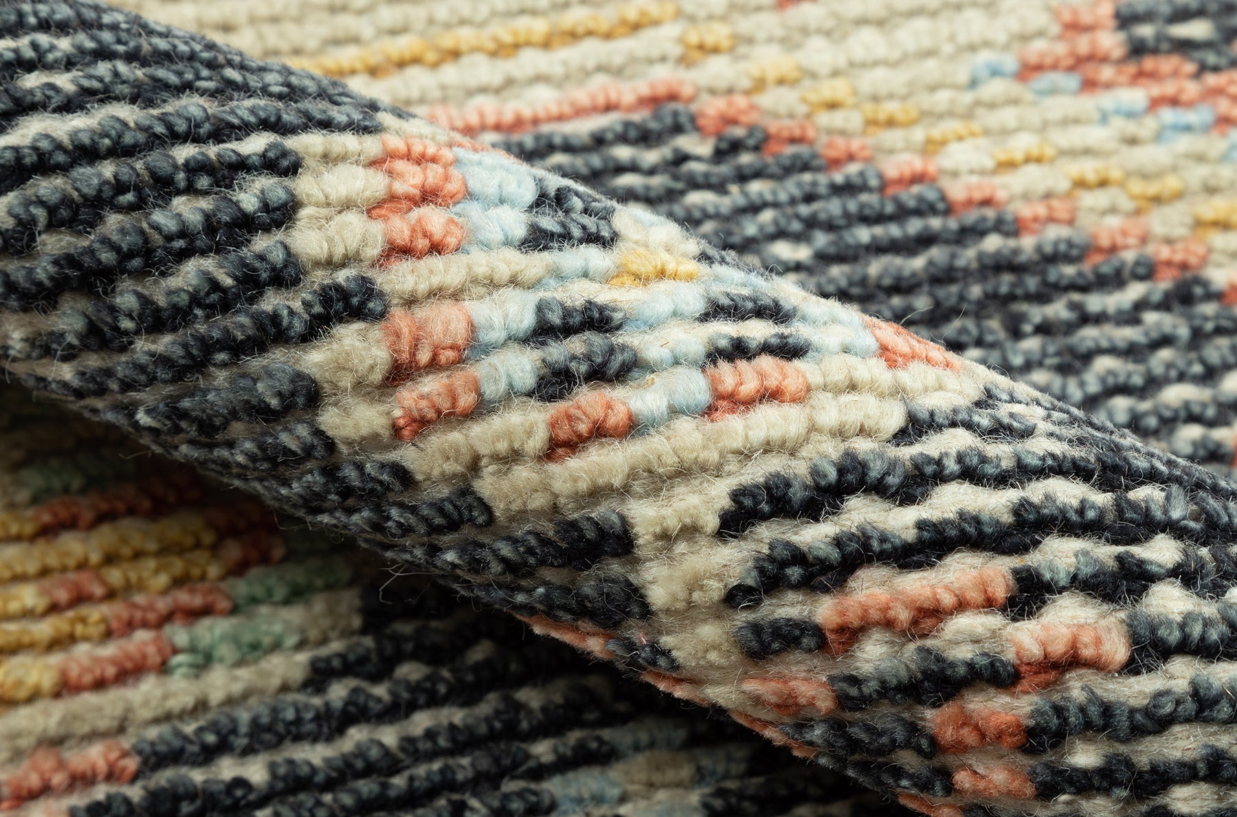Close-up of a handwoven rug with dark navy, cream, peach and light blue geometric pattern; thick looped pile.