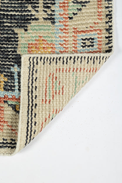 Beige oriental rug with multicolor geometric motifs in navy, teal and red; woven texture with folded corner.