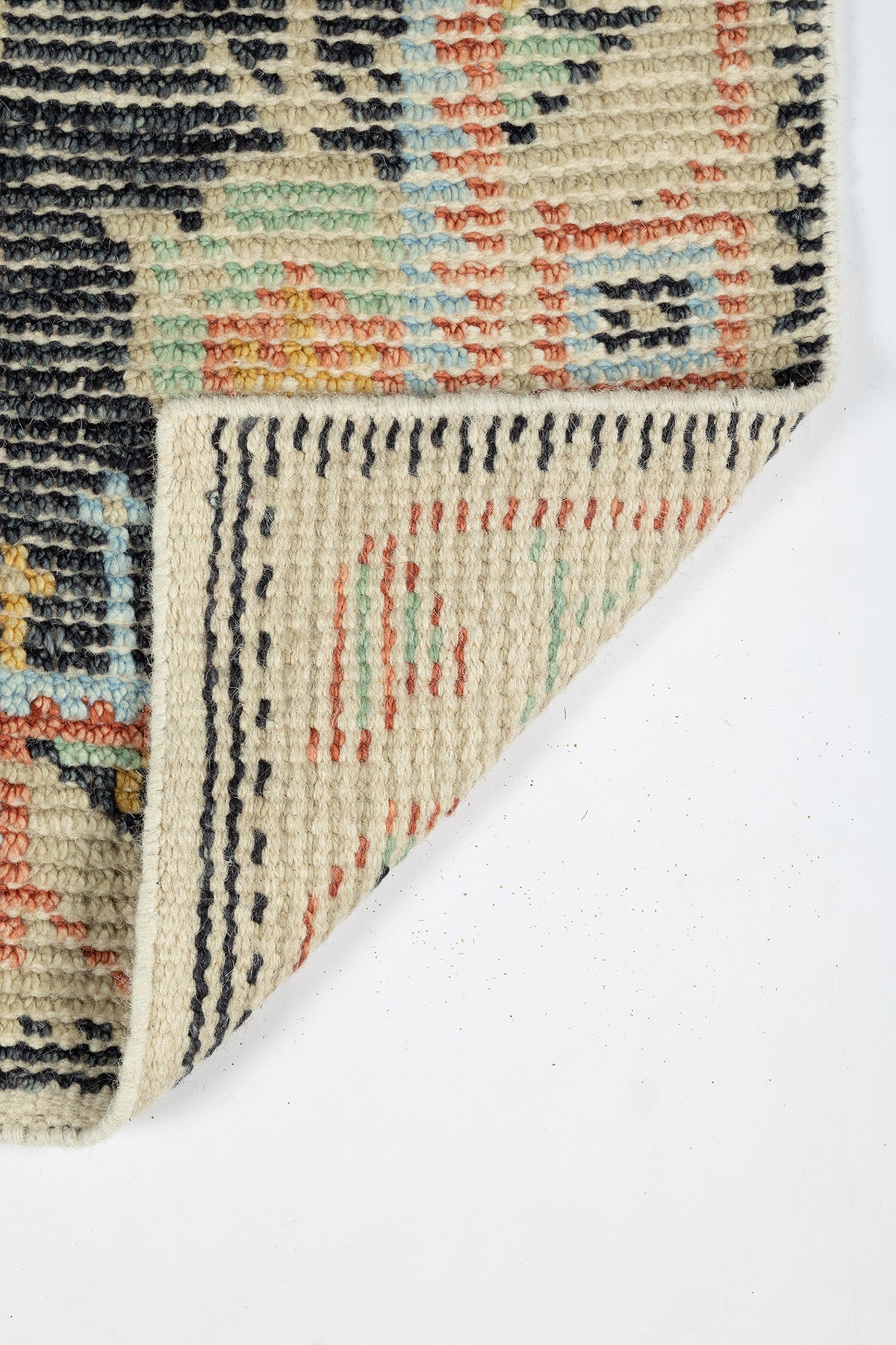 Partial view of beige Oriental rug with geometric multicolor pattern, blue, red & green; folded corner.