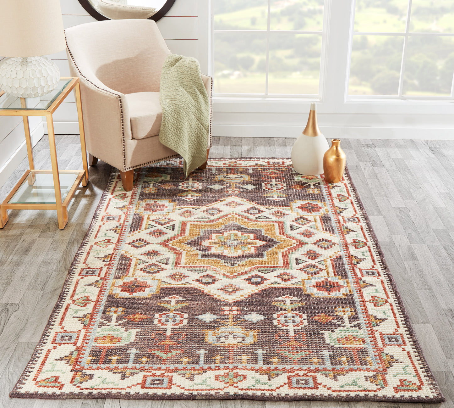 Geometric oriental area rug in warm browns, creams, rust and teal; pairs with beige armchair and gold-toned decor.