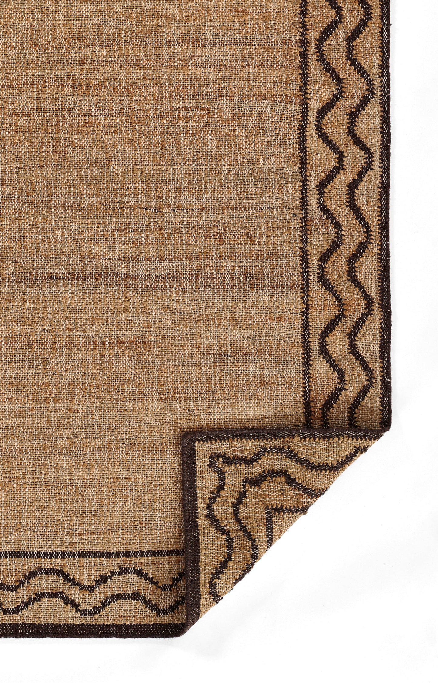 Natural jute rug in tan with dark brown border and wavy edge; folded corner shows textured weave.