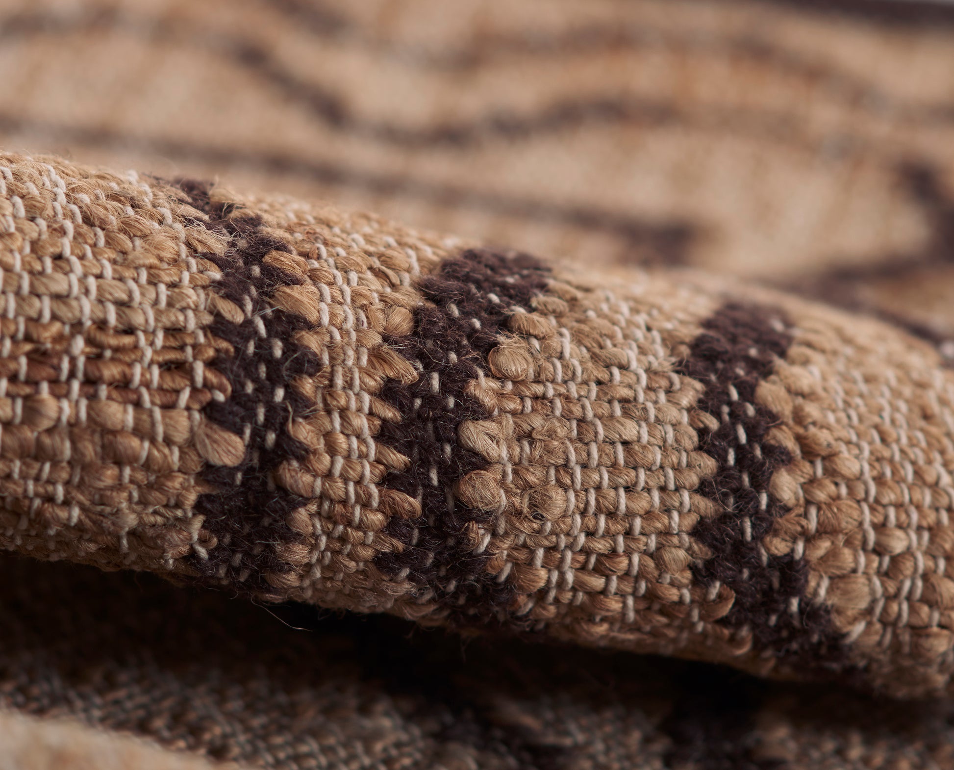 Close-up of a beige-brown woven rug with dark brown geometric stripes; chunky weave & natural fibers.
