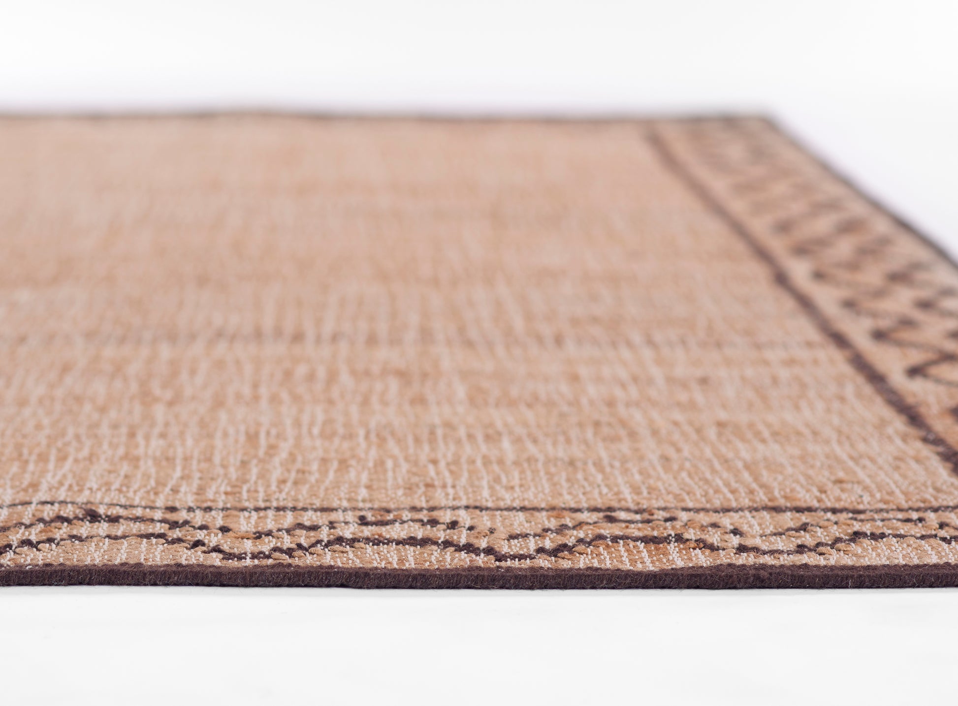 Rectangular natural fiber rug in tan with dark brown geometric border; woven texture.