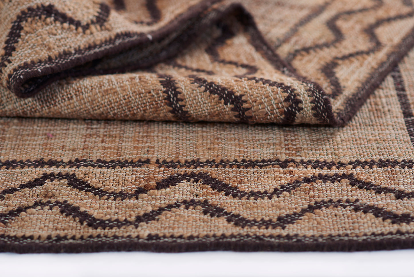 Natural beige-brown woven rug with dark brown chevron geometric pattern and folded corner.