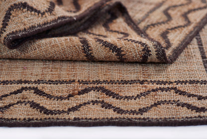 Tan and brown woven rug with dark brown geometric diamond pattern and textured jute-like fibers.