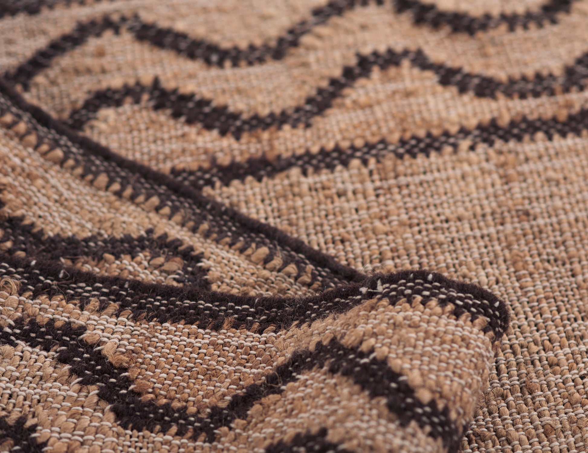 Tan and dark brown woven rug with geometric diamond patterns and textured fibers.