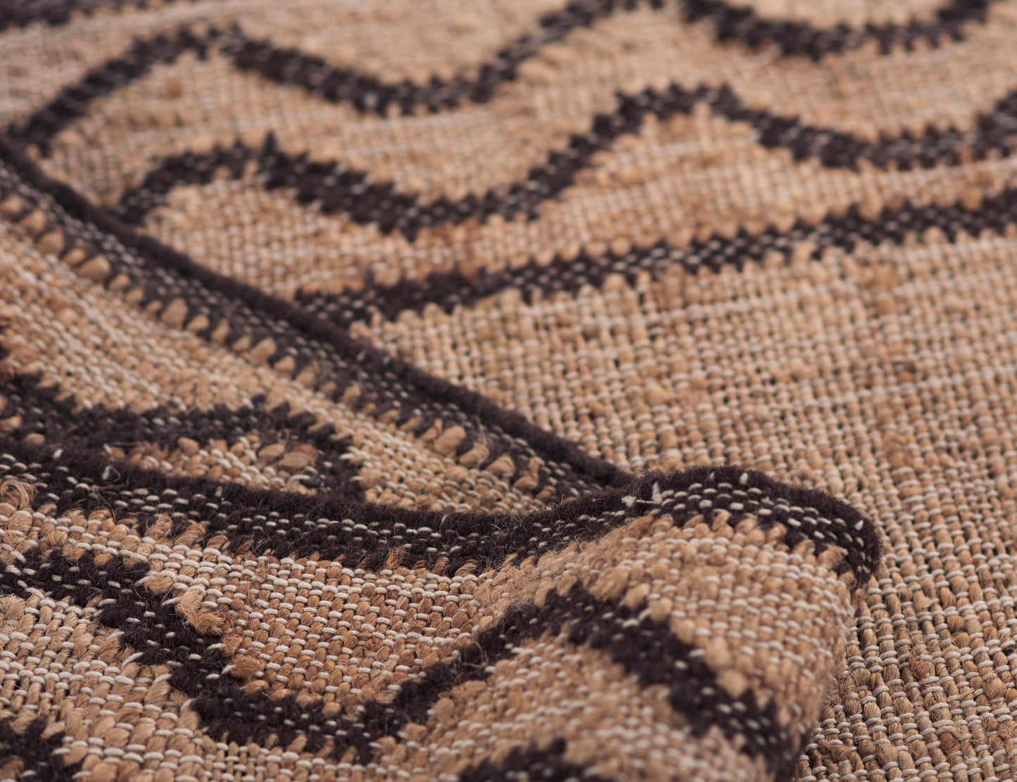 Beige woven rug with dark brown geometric diamond pattern, chunky textured fibers, rustic style.