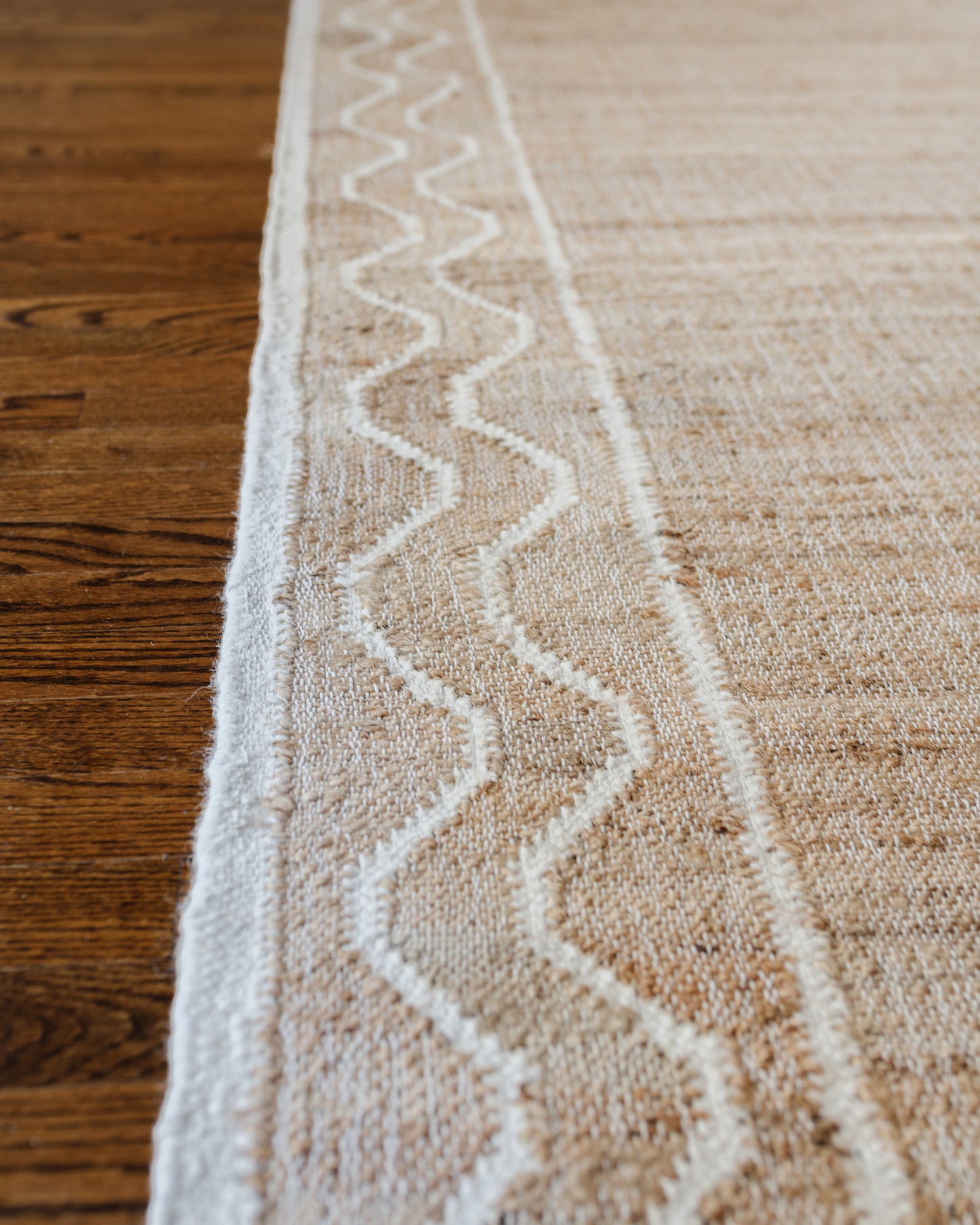 Beige natural-fiber rug with a white zigzag border along the edges, laid on a wooden floor, 8' x 10'.