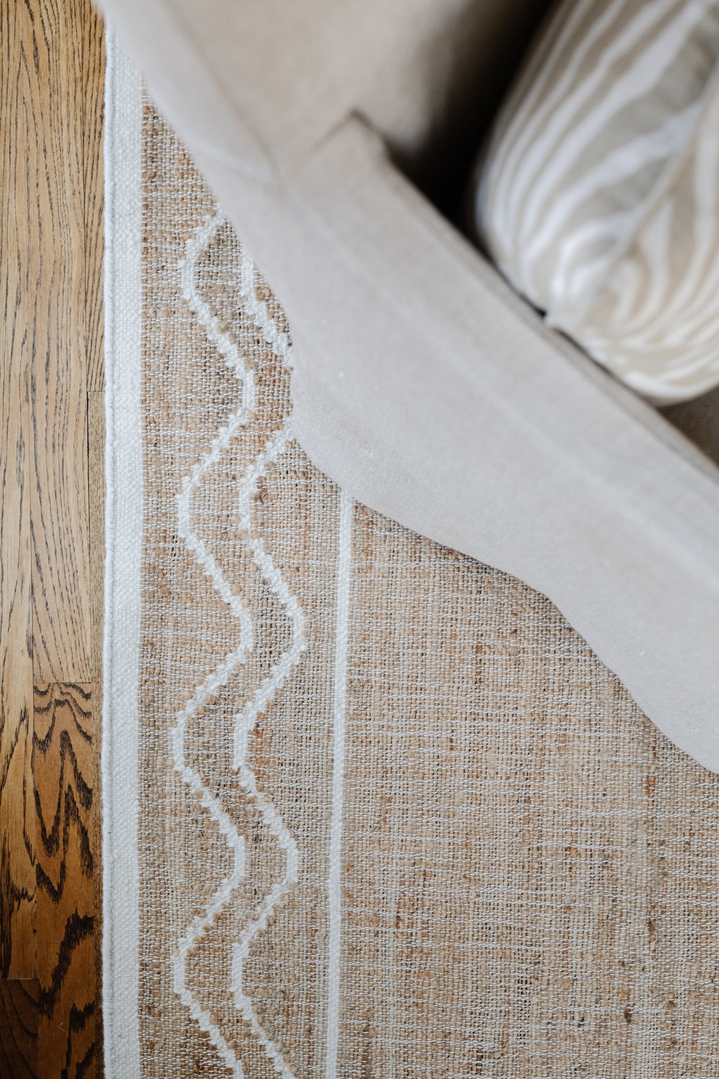 Natural jute rug with white wavy border, beige woven texture, on wood floor beside a light sofa.