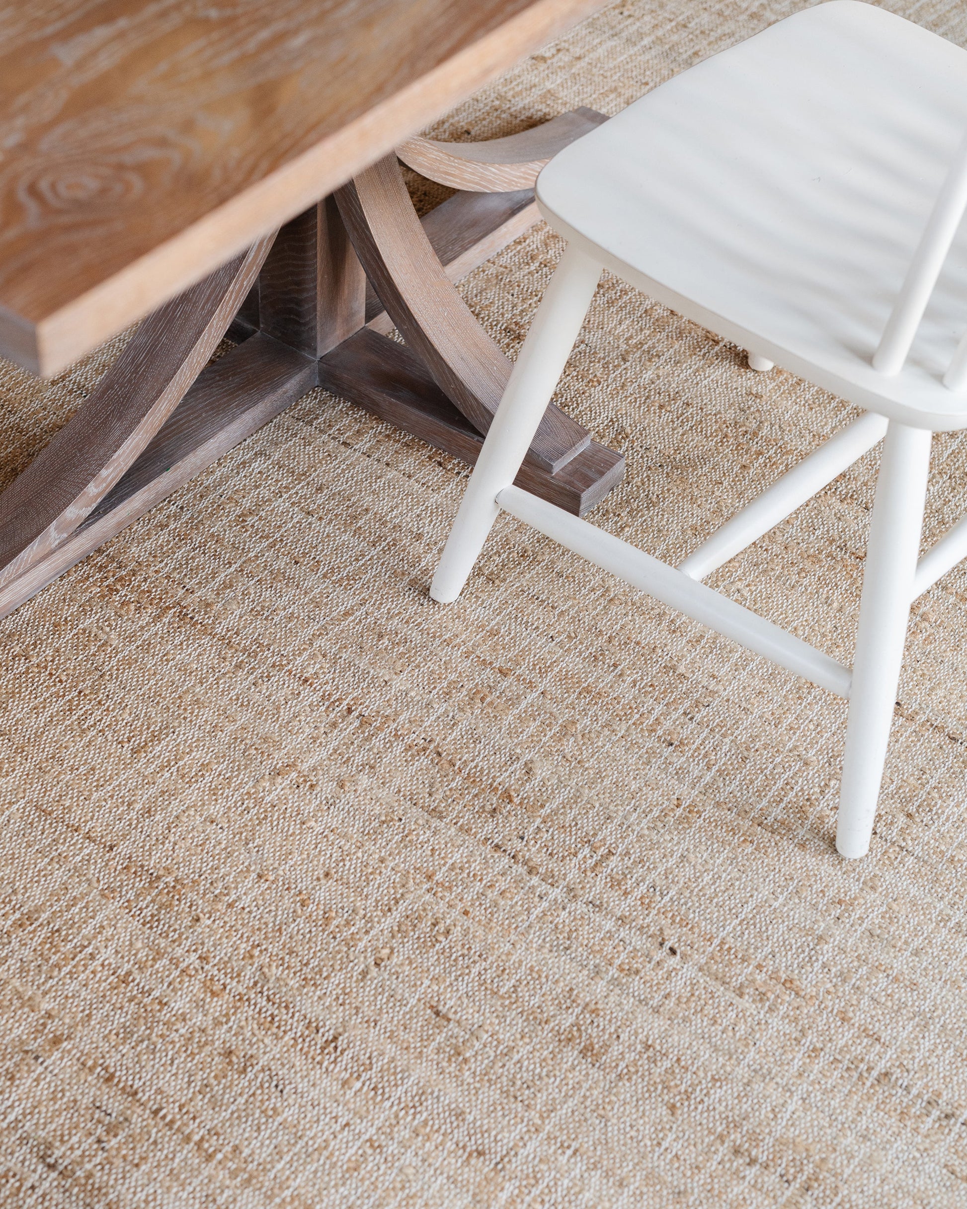 Beige woven rug with a white painted wooden chair beside a rustic brown wooden table.