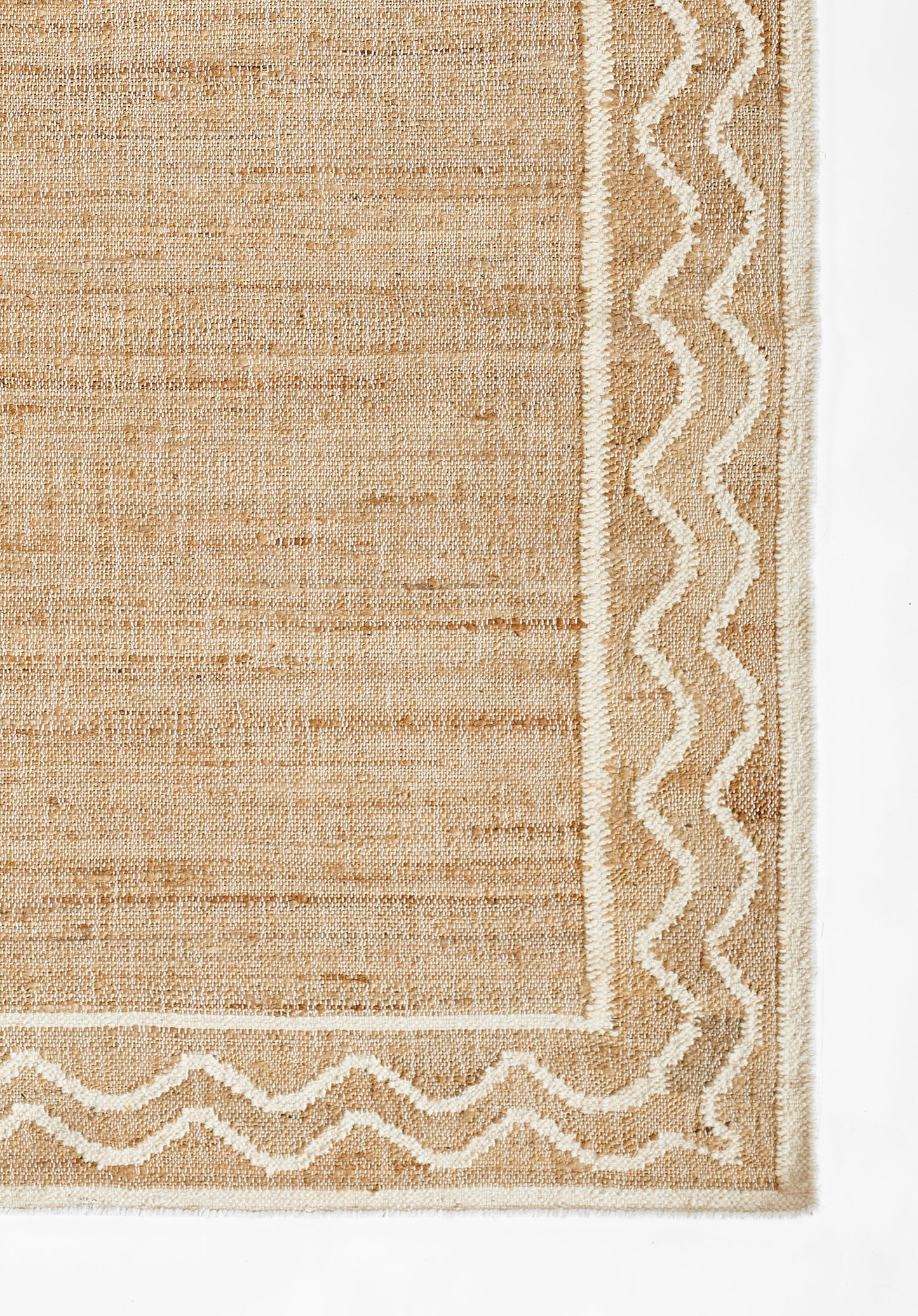Natural beige woven rug with a white zigzag border and textured, coarse fiber surface.