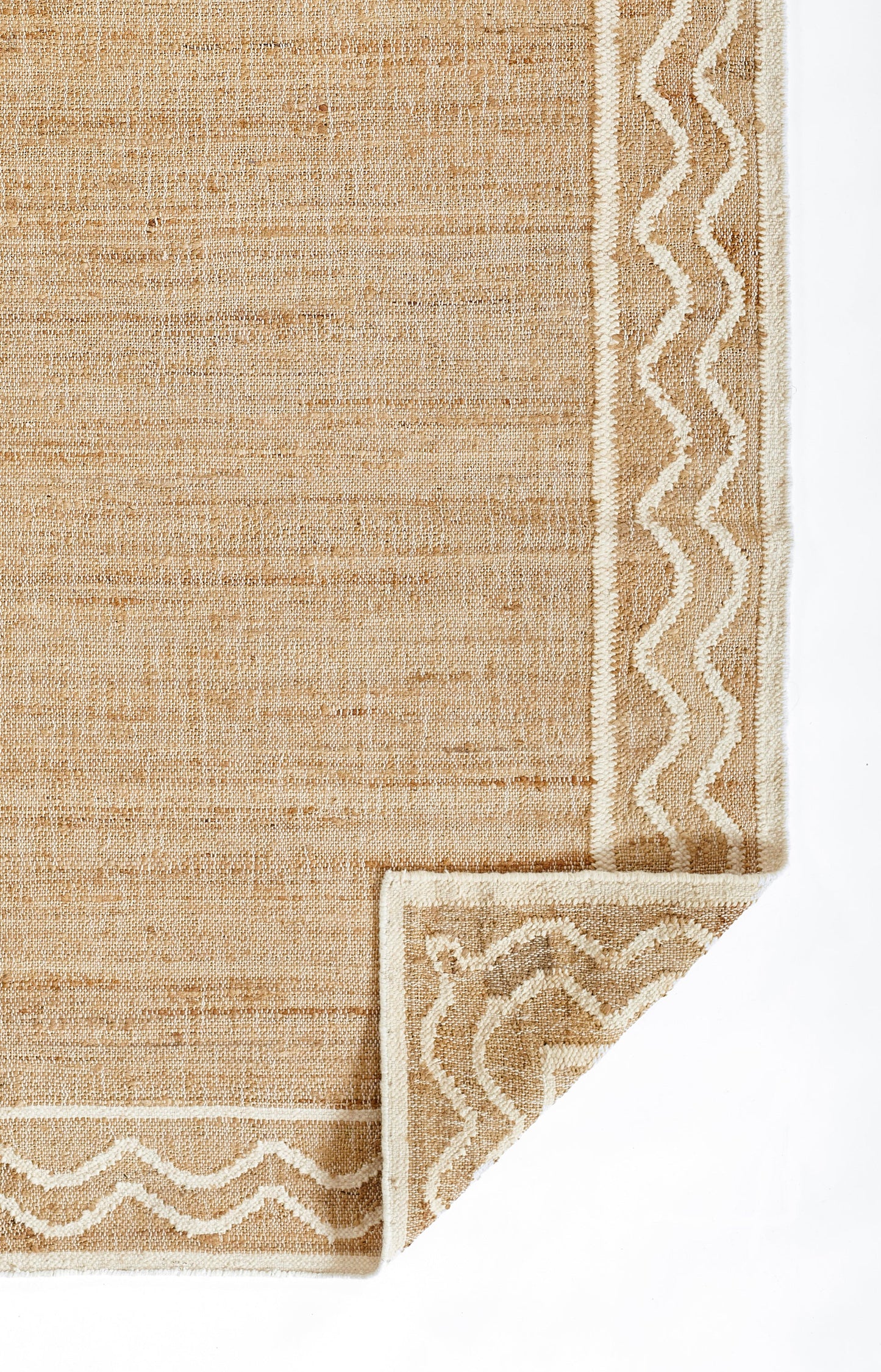 Beige woven rug with a white chevron border and folded corner detail.