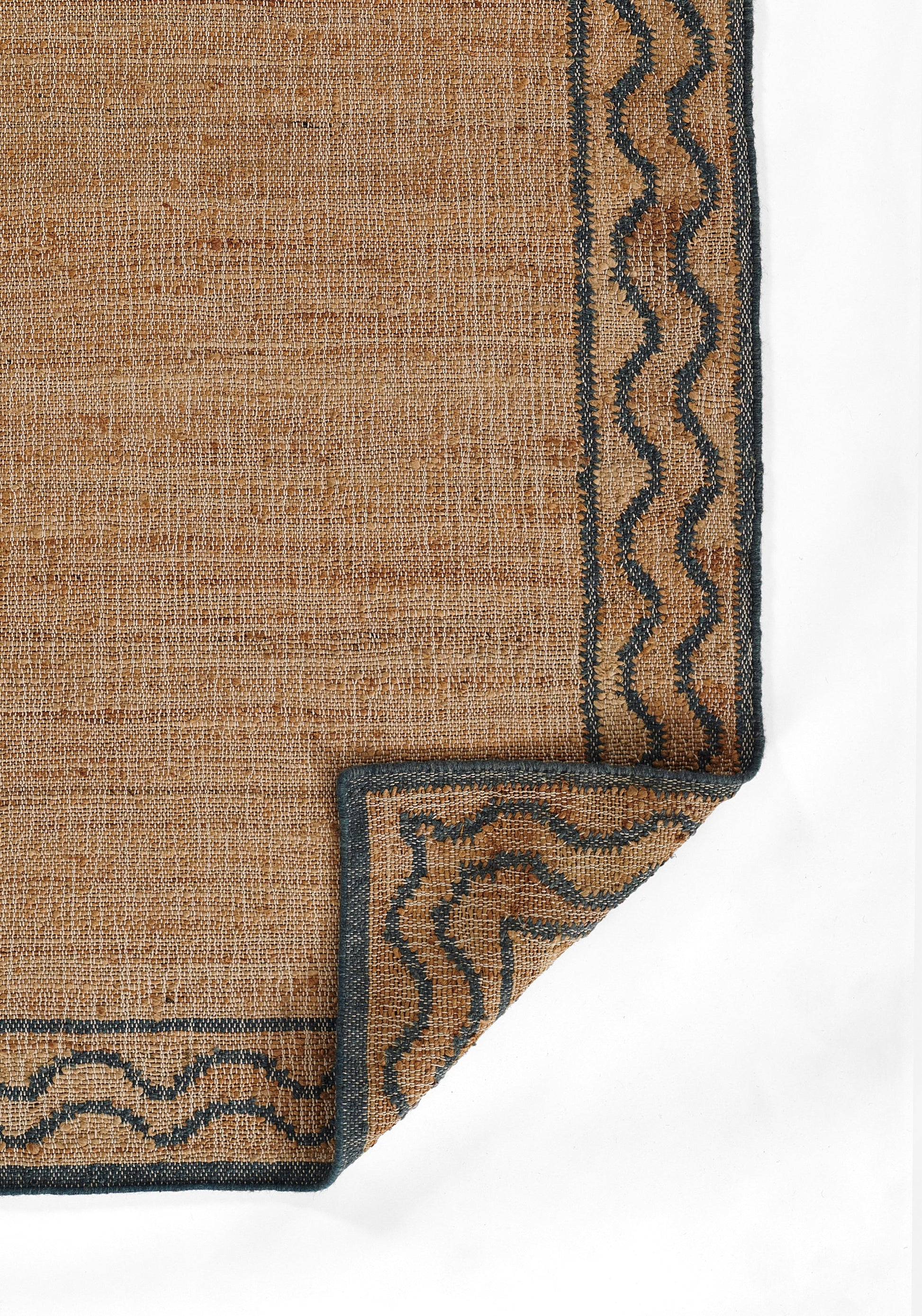 Natural brown jute rug with dark blue border and zigzag wavy trim; folded corner reveals underside.