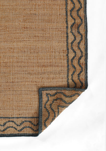 Natural tan jute rug with dark blue wavy border and folded corner.