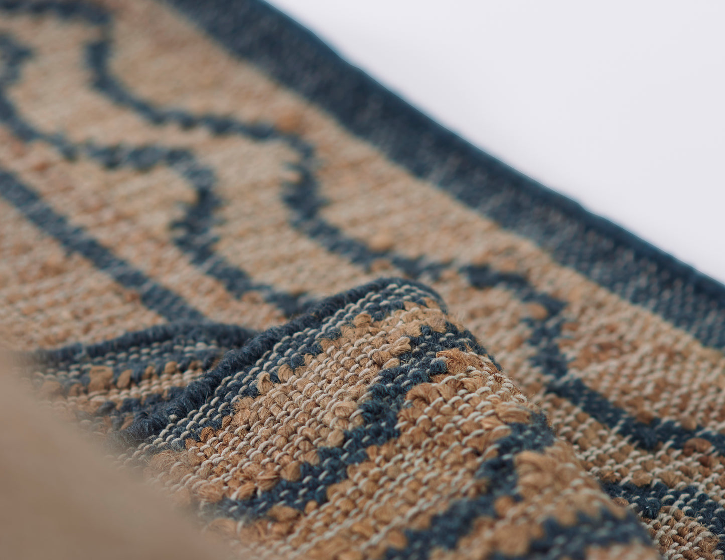 Close-up of blue and tan geometric woven rug with chunky textured fibers and folded edge.