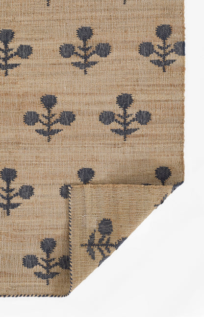 Natural jute rug with navy blue floral motifs, woven texture, and blue braided edge; corner folded.