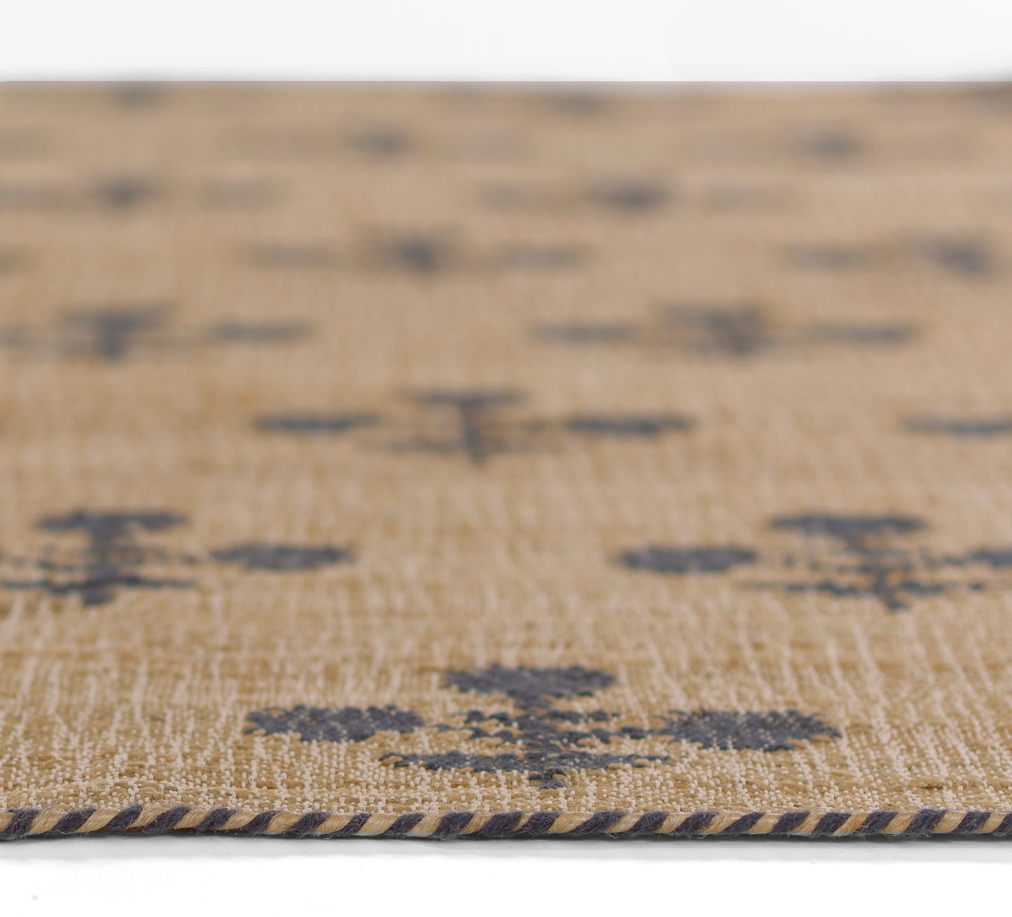 Beige woven rug with dark blue abstract patches and a navy braided edge.