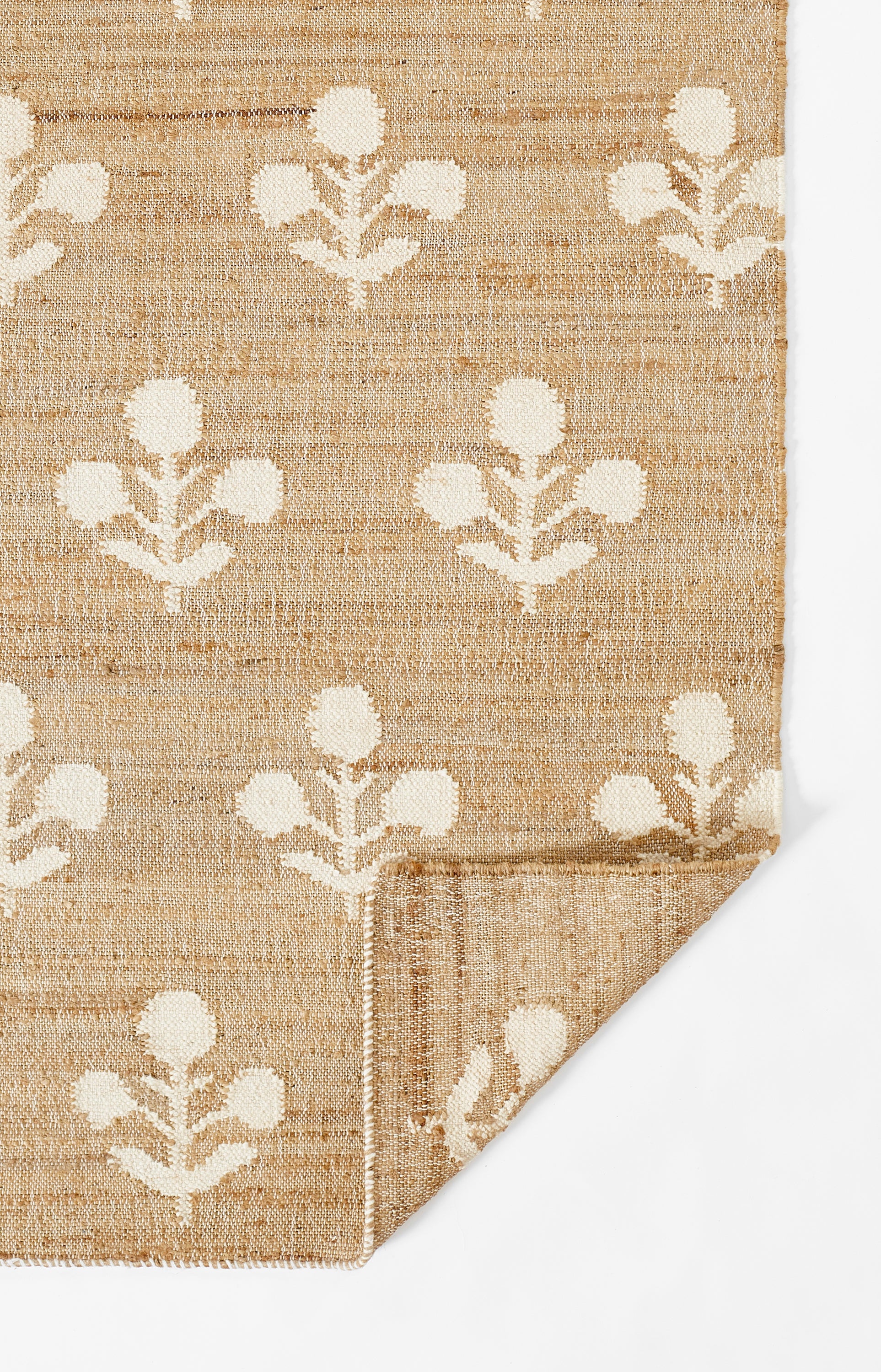 Beige jute rug with white botanical leaf pattern, folded corner.