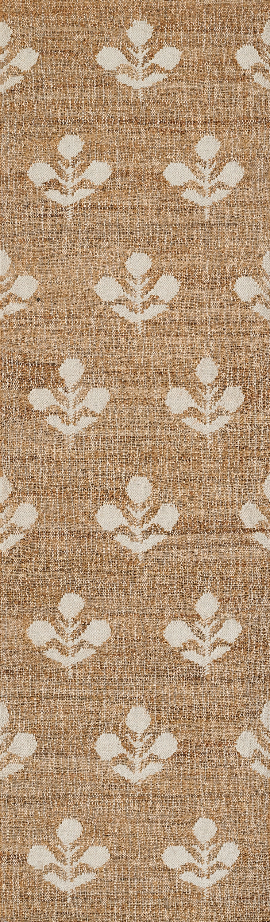 Tan woven rug with white floral leaf motifs in a repeating pattern; rustic natural fiber look.