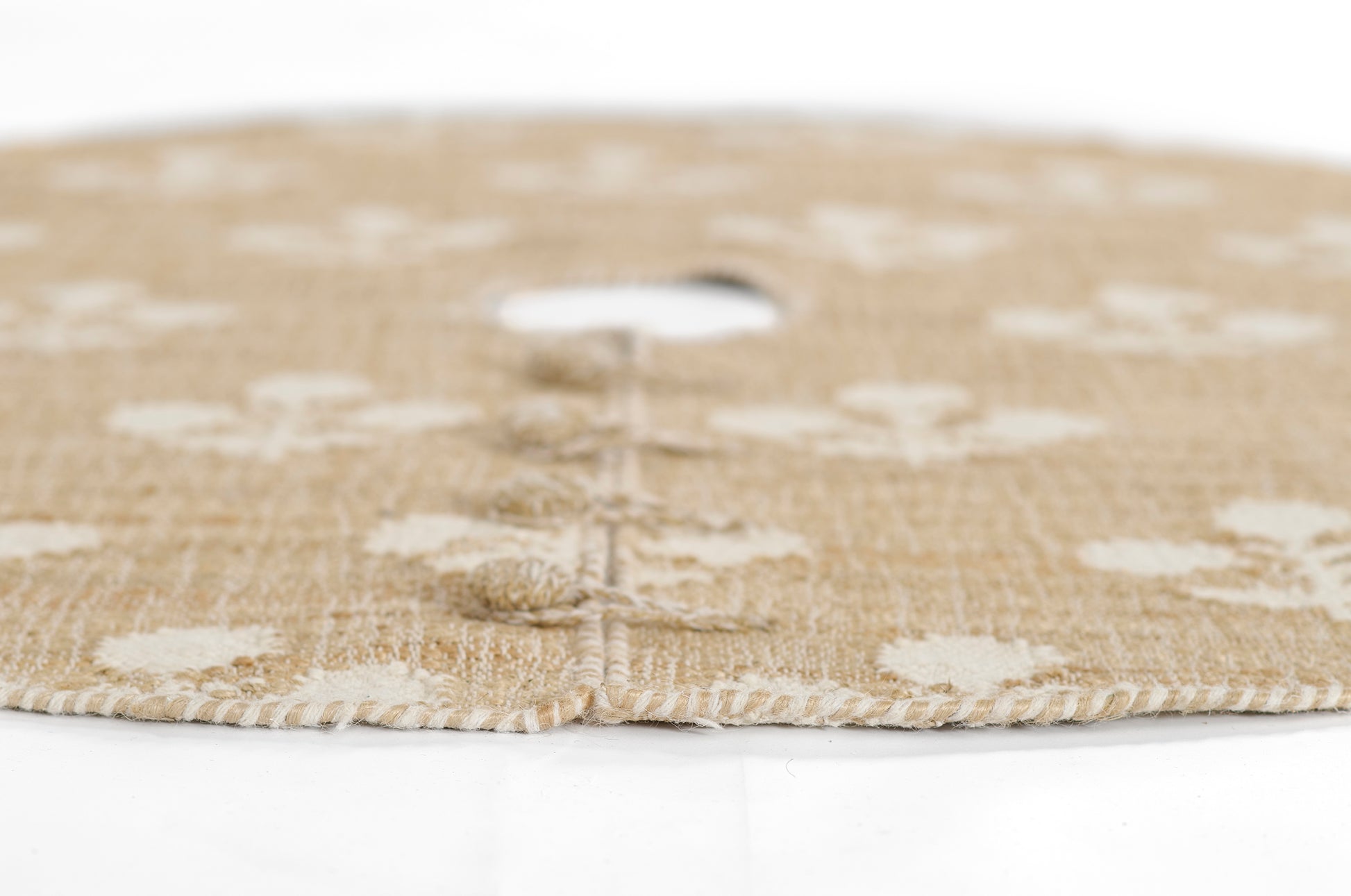Natural beige jute round rug with white floral motifs and braided edge, 5' diameter.