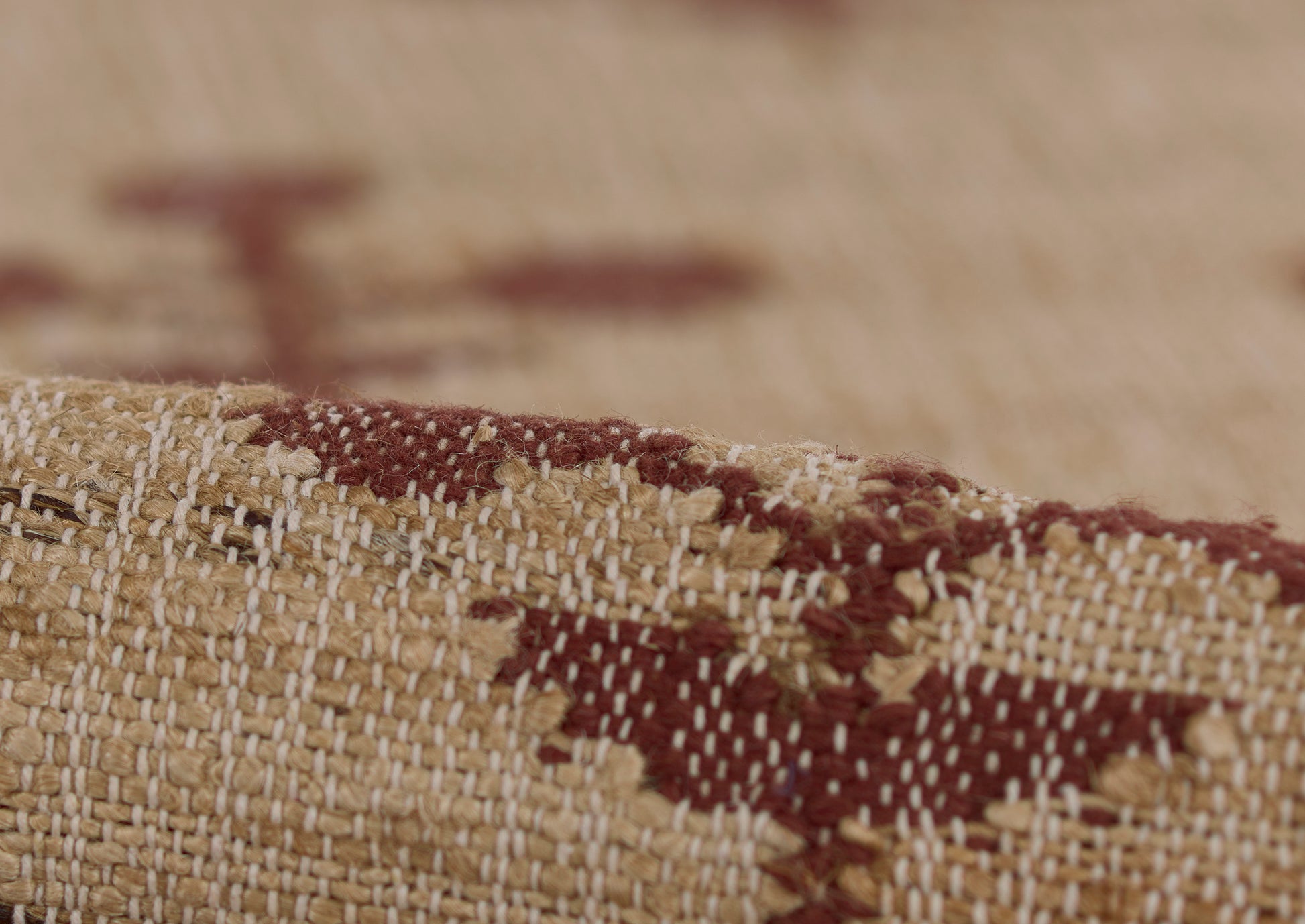 Close-up of a beige and burgundy woven rug with a geometric pattern and a rolled edge.