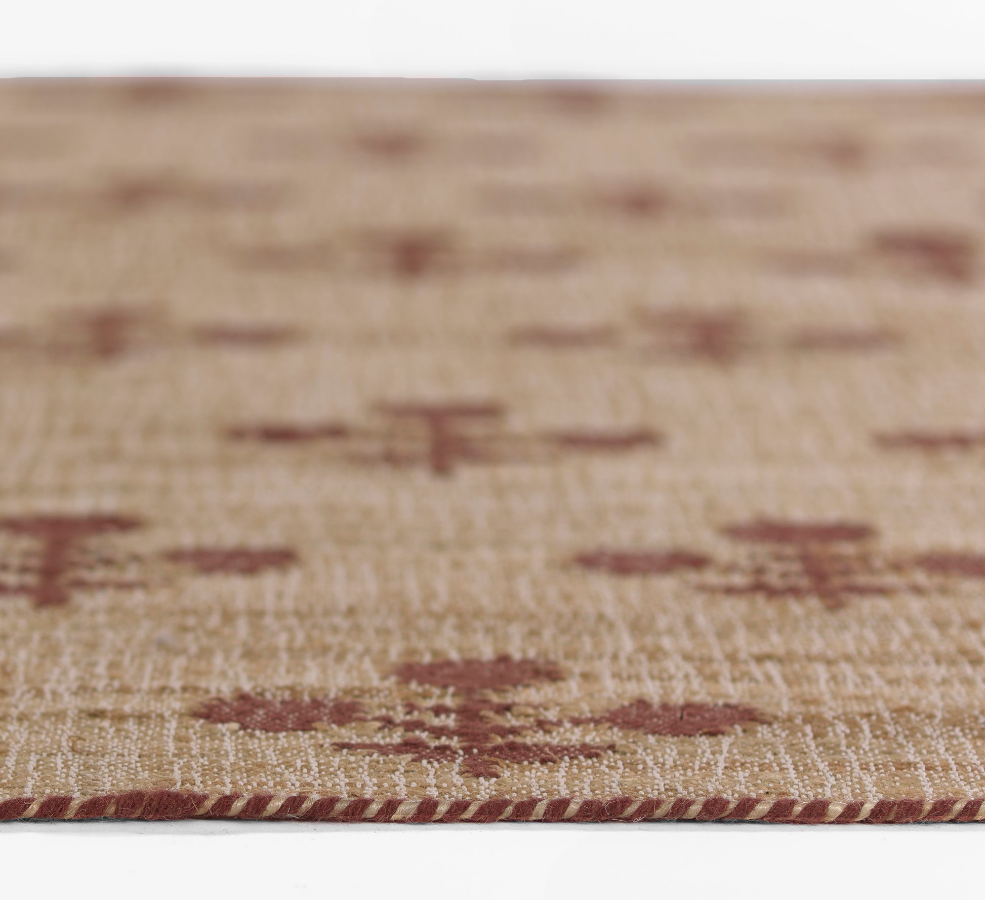 Close-up of a beige woven rug with burgundy diamond motifs and a red braided edge