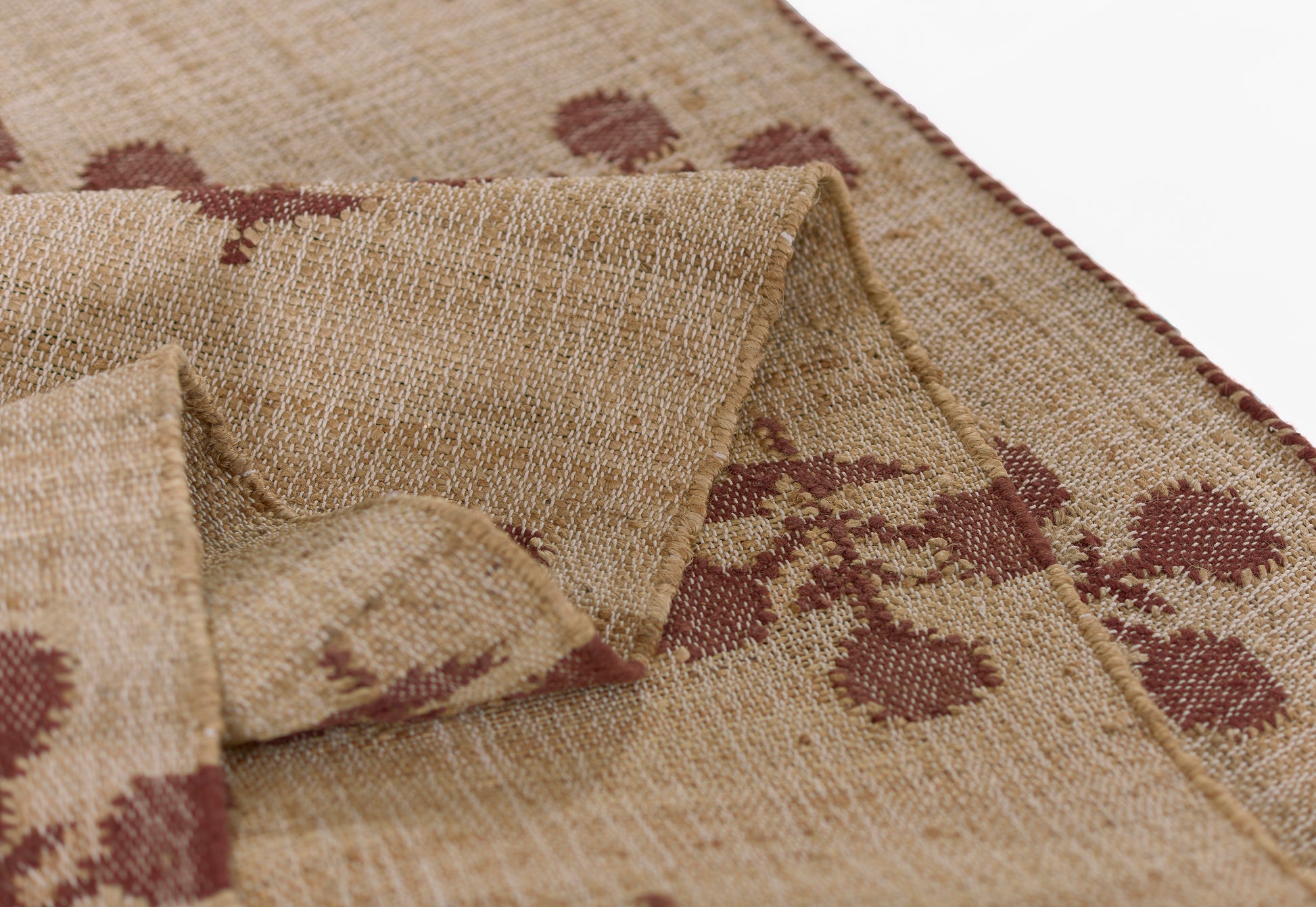 Natural beige woven rug with burgundy floral pattern, rustic jute texture, rolled edge.