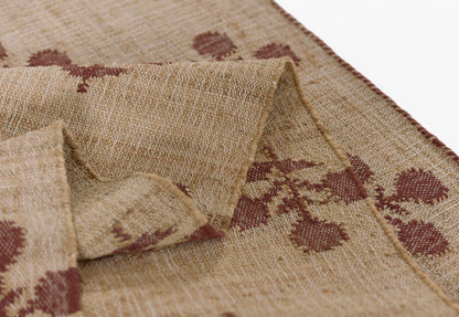 Natural burlap-style rug with maroon floral motif; folded edge shows coarse woven texture.