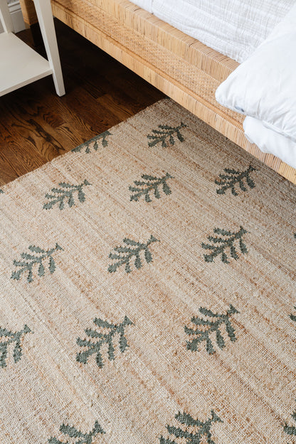Natural jute rug with green fern motifs on beige woven texture.
