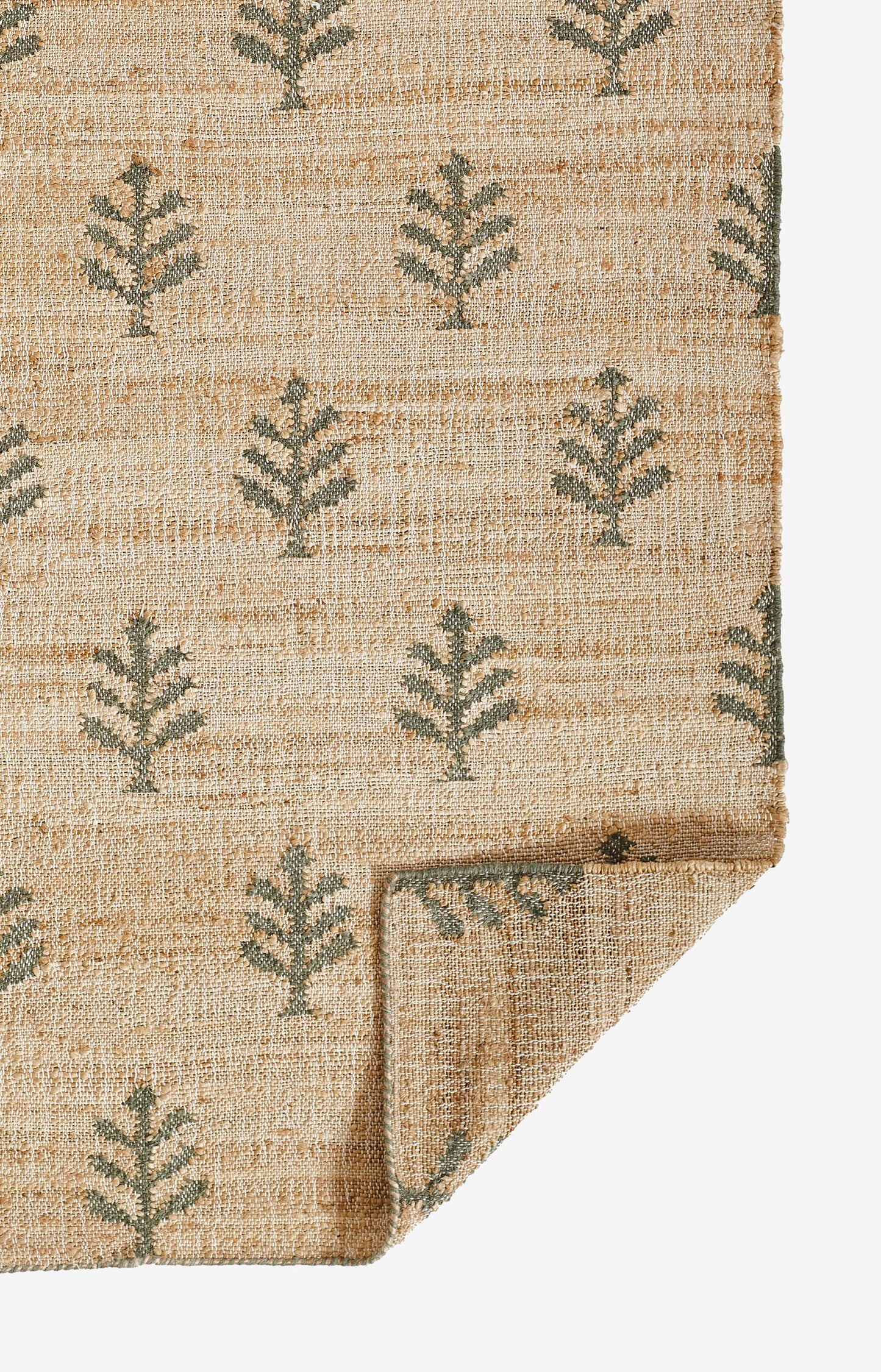 Natural jute rug & green leaf/fern motifs on beige textured weave; rectangular & folded corner.