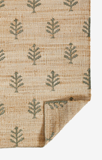 Natural beige woven rug with green fern-like motifs, folded corner showing edge detail.