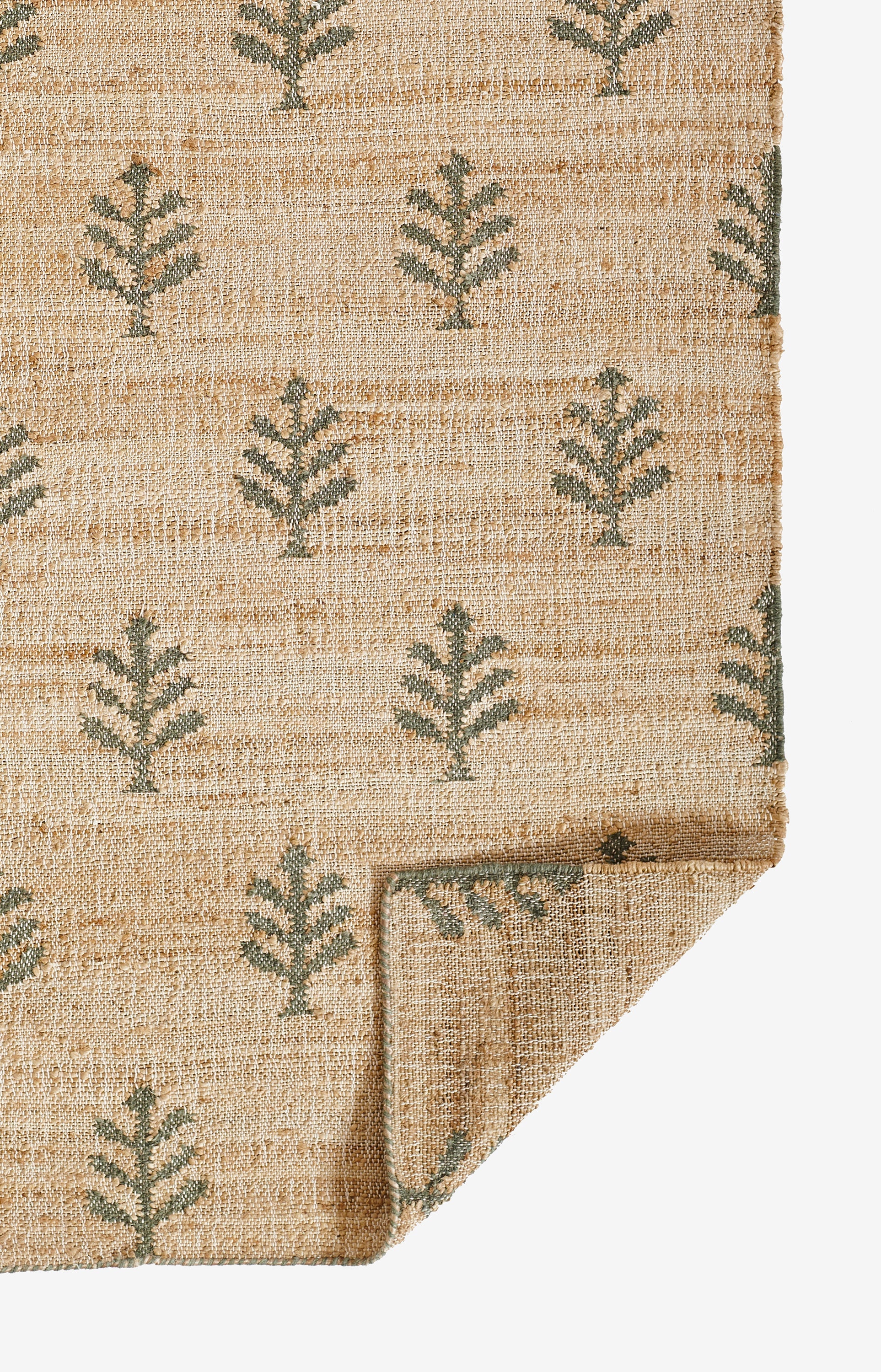 Natural beige jute rug with green fern patterns; rustic rectangular rug, folded corner visible.