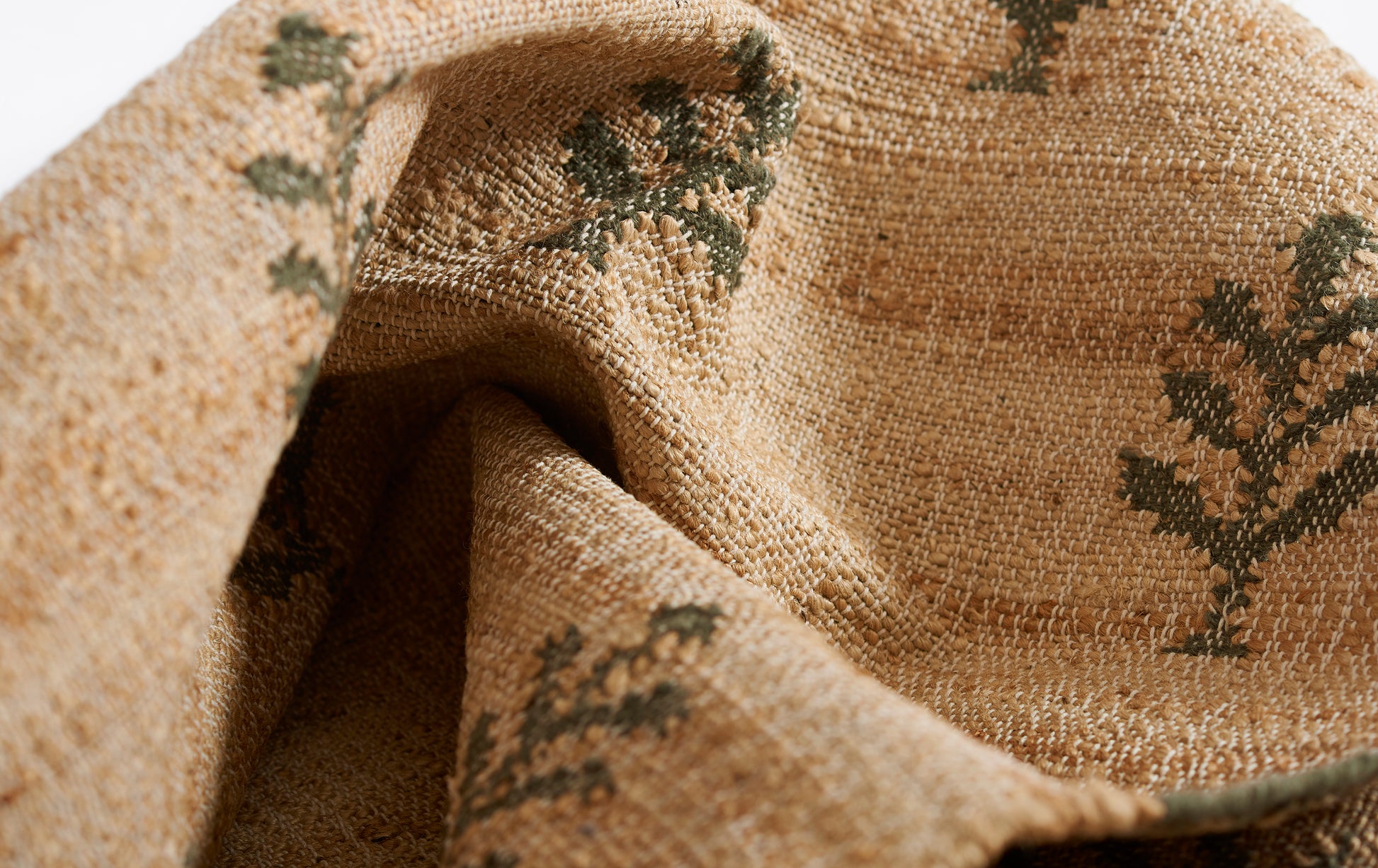 Natural beige woven jute rug with dark green leaf motifs & textured rustic look.