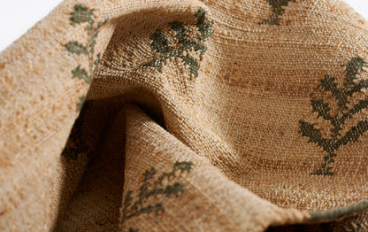 Natural beige woven jute rug with dark green leaf motifs & textured rustic look.
