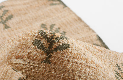 Natural beige woven rug fabric with a green botanical motif and chunky textured fibers.