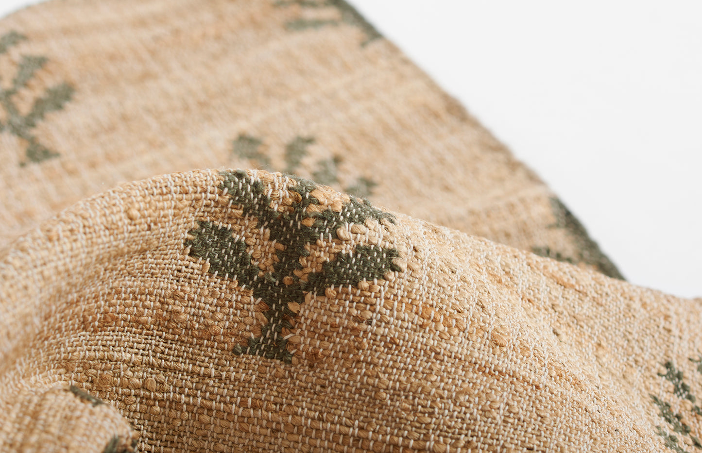 Natural beige woven jute textile with olive green leaf motif and textured surface.