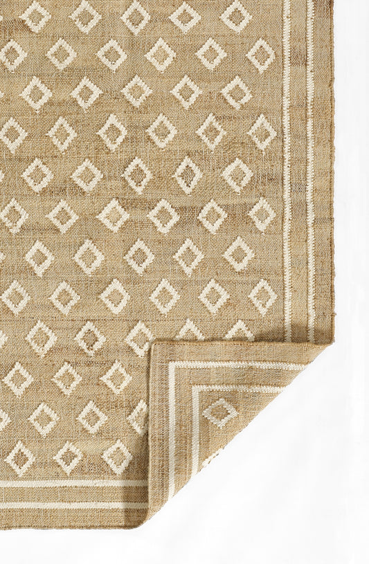 Beige natural-fiber rug with white diamond geometric pattern, bordered edges, folded corner.
