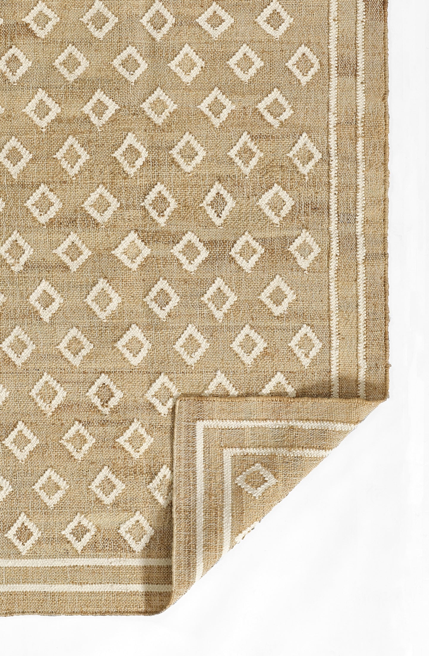 Natural beige woven rug with white diamond geometric pattern and striped border, folded corner.
