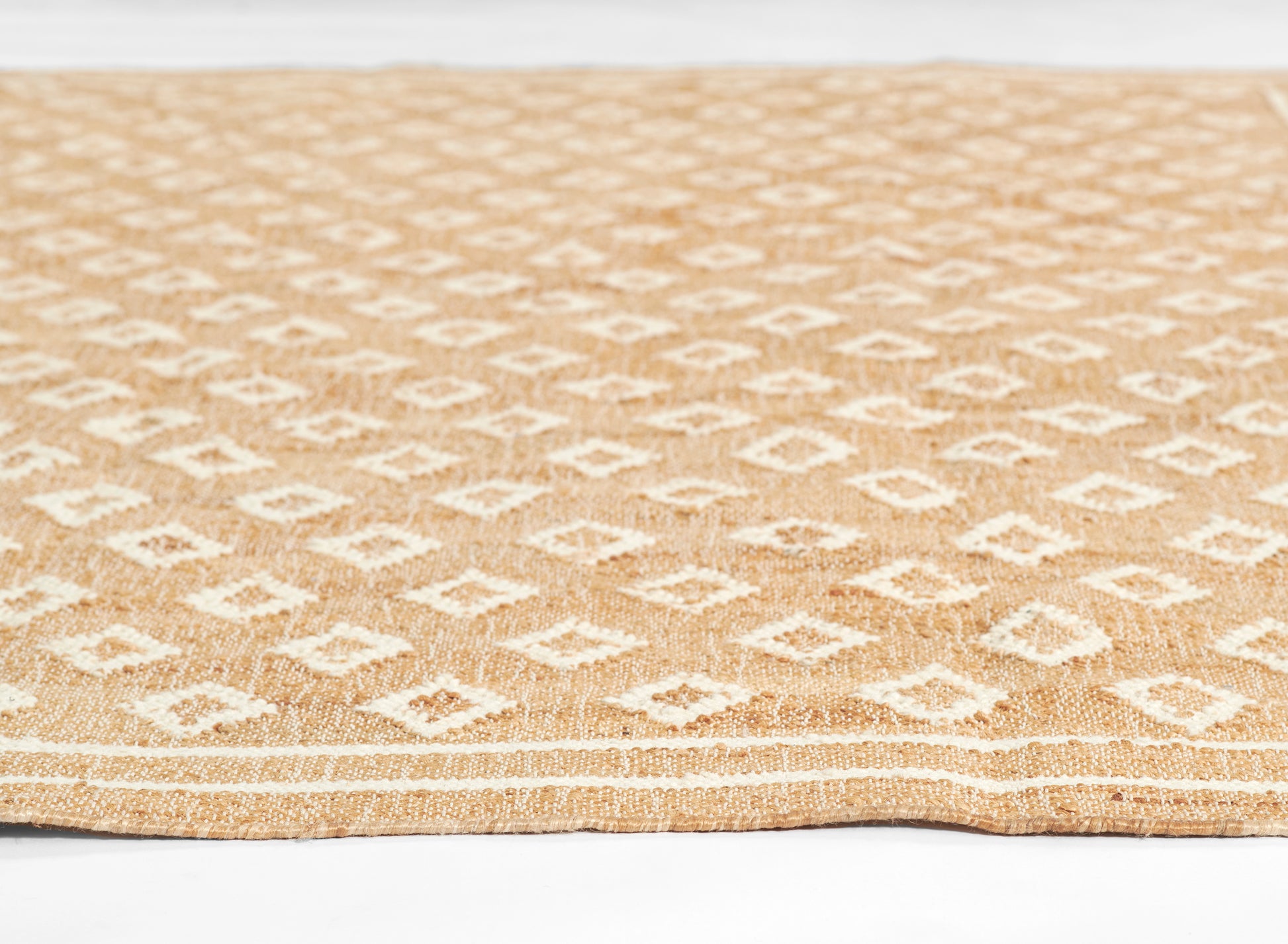 Natural jute rug with white diamond geometric pattern on tan background; rectangular, boho coastal style.