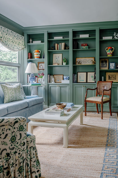 Teal built-in shelves with display cabinets flank a cozy living room; blue sofa, white coffee table, wooden chair, beige rug.