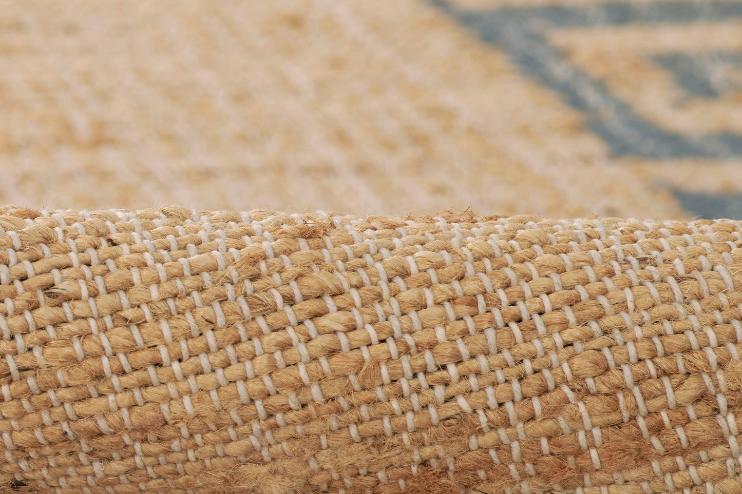 Close-up of natural jute rug roll with tan fibers and blue Greek Key pattern accents.